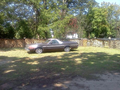 1979 Ford Ranchero - A brown 1979 Ford Ranchero pickup truck is parked on a grassy lawn with a woodpile fence in the background.