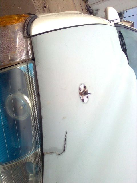 1984 Ford Bronco - Detail of a white vehicle's hood and headlight assembly, showing some damage.
