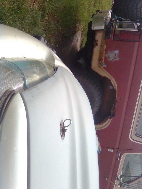 1984 Ford Bronco - Two vehicles are parked closely together, one white and one red, with visible rust on the red vehicle's fender.