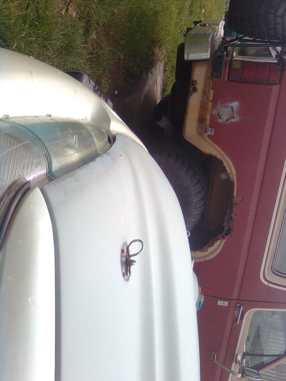 Close-up of a white vehicle's fender next to a red vehicle's side, showing rust and a spare tire