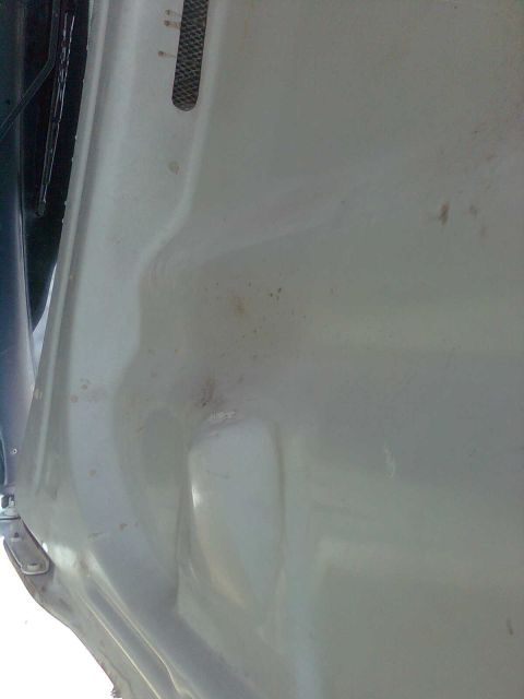 1984 Ford Bronco - Close-up of a dented white car hood with a black vent detail.