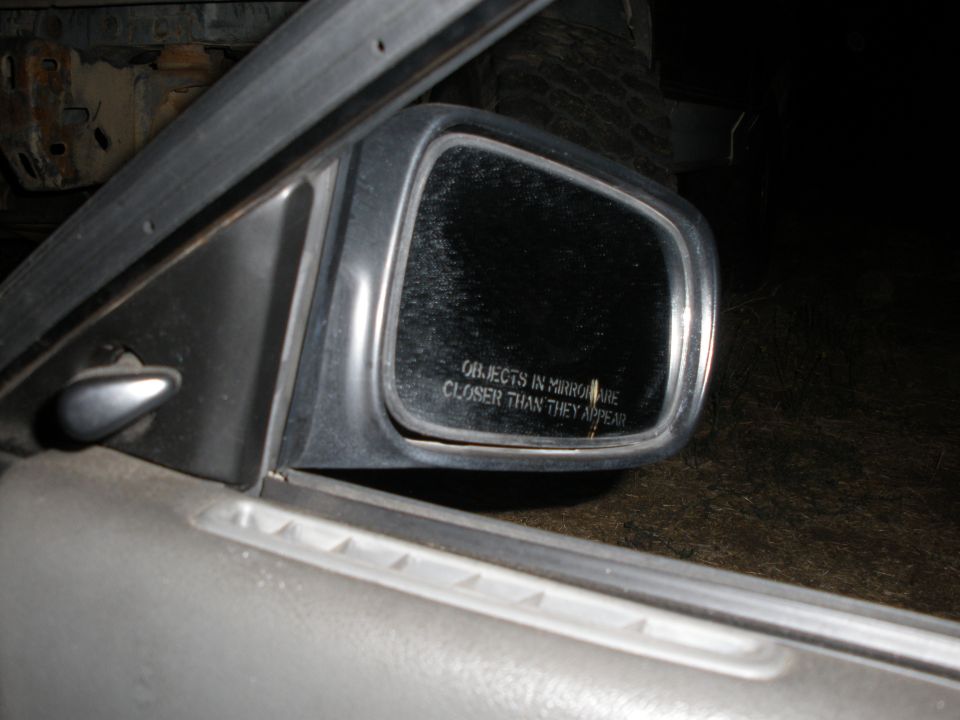 Passenger door mirror with warning etching on a silver car door, window down, at night