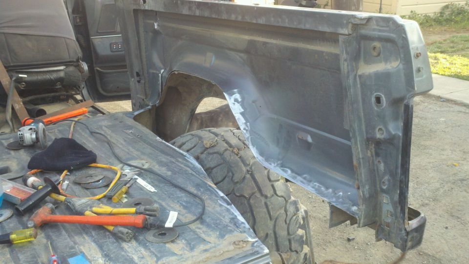 Ford Bronco interior with tools and disassembled bed panel. Gray interior, black fabric seat, metal bed, tire visible
