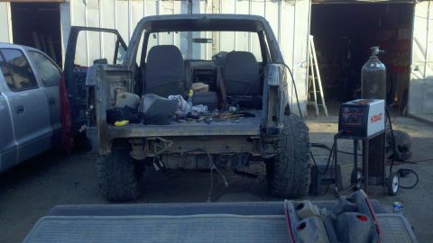 1989 Ford Bronco - This SUV is missing its body panels and appears to be undergoing repairs or modifications, with welding equipment set up next to it.