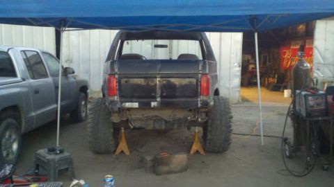 1989 Ford Bronco - Rear view of a modified black Ford Bronco on jack stands, with another truck parked nearby.