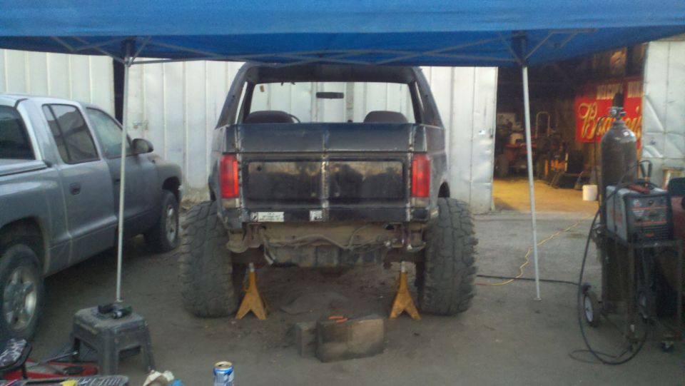 Black Ford Bronco on jack stands, rear view, modified bumper, large tires