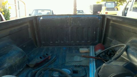 1989 Ford Bronco - View from inside the bed of a pickup truck, showing various items and other vehicles in the background.