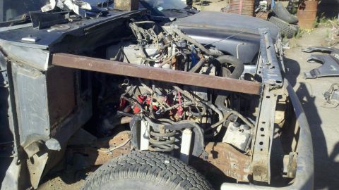 1989 Ford Bronco - The engine bay of a heavily damaged vehicle, showing exposed wiring and suspension components.