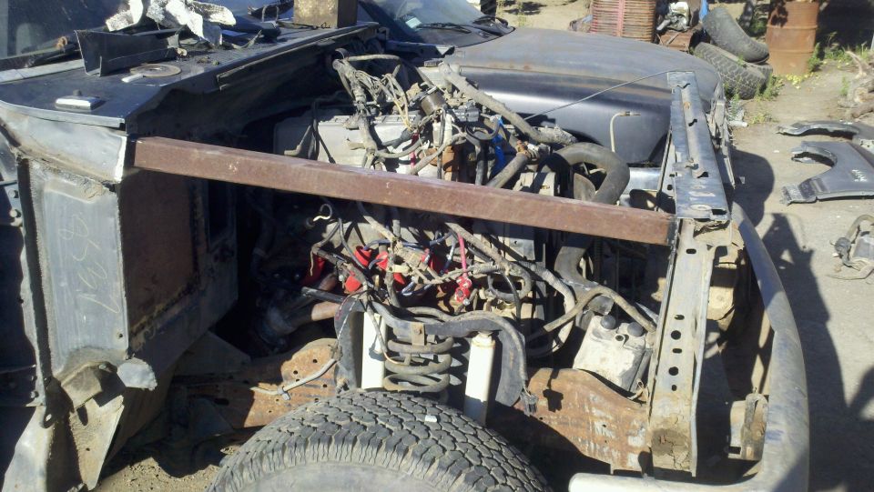 Junked vehicle with engine exposed and a metal bar across the engine bay