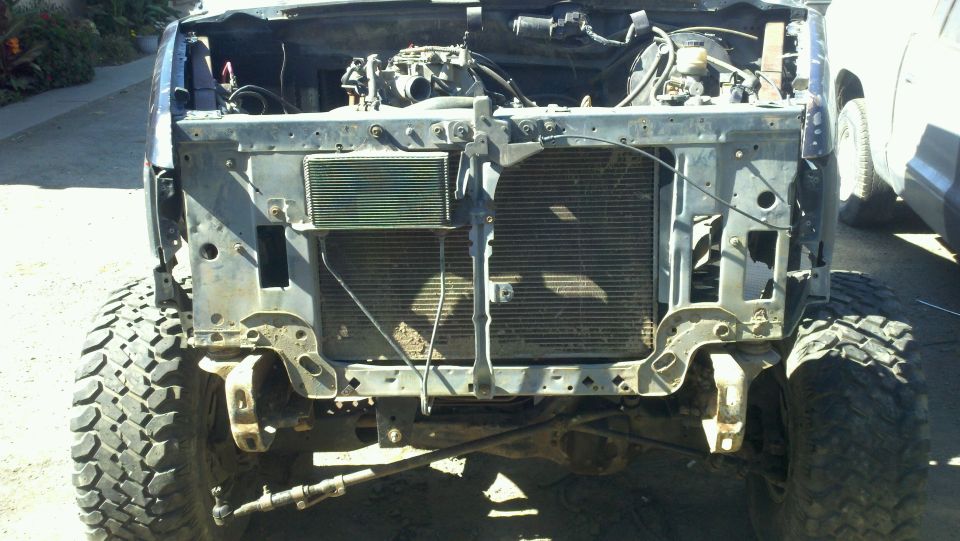 Front end of a disassembled SUV, showing the radiator and engine components. Large off-road tires are visible