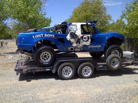 1995 Ford Bronco - A blue off-road truck with a skull graphic and 'LOST BOYS' text is loaded onto a trailer.