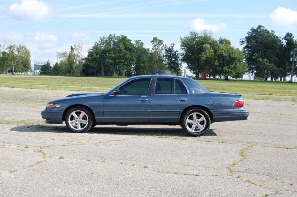 Blue sedan with tinted windows and aftermarket wheels parked on cracked pavement