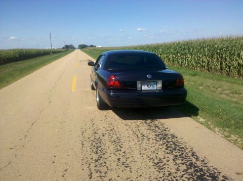 1999 Mercury Grand Marquis - A dark sedan is parked on the side of a road bordered by cornfields under a clear blue sky.