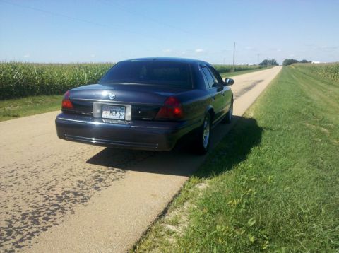 1999 Mercury Grand Marquis - A dark blue sedan is parked on the shoulder of a rural road, with cornfields on either side under a clear blue sky.