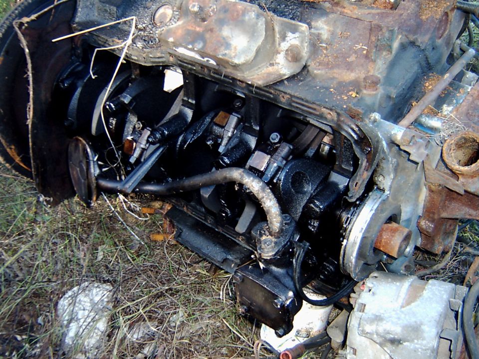 Rusty V8 engine block lying in grass with heads removed and flywheel exposed