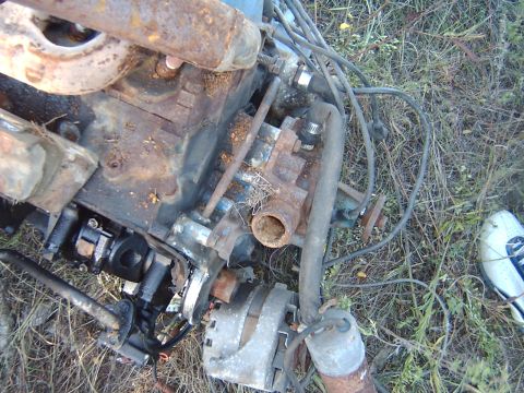 1982 Ford Bronco - This is a close-up view of a rusty engine block and alternator, partially covered in dirt and debris.
