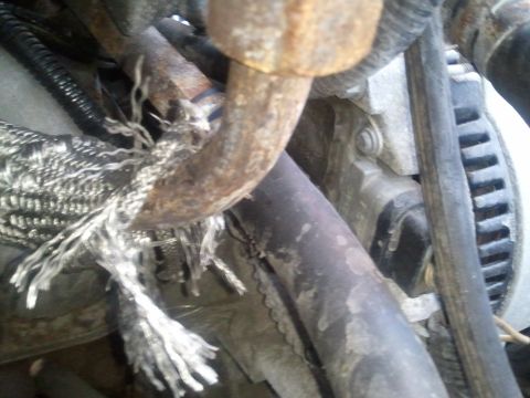 1994 Ford Bronco - Close-up view of a damaged engine component with frayed insulation and a rusty pipe, suggesting wear and tear.