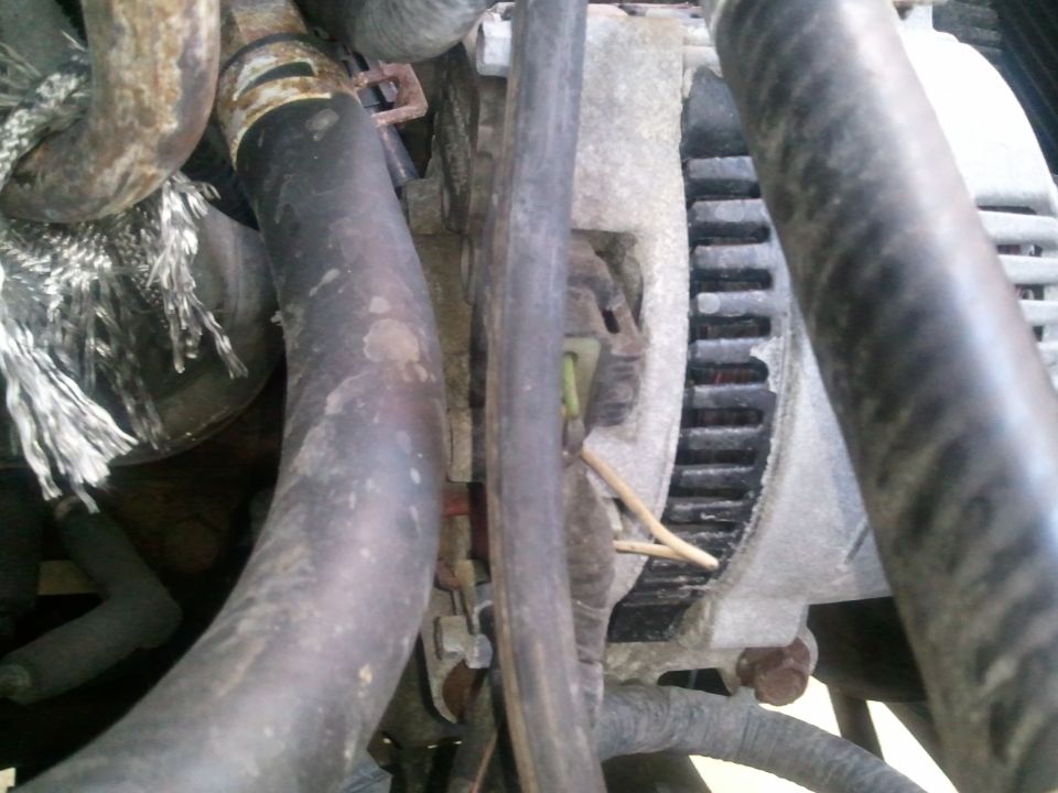 Close-up of a vehicle's alternator with black hoses and frayed insulation