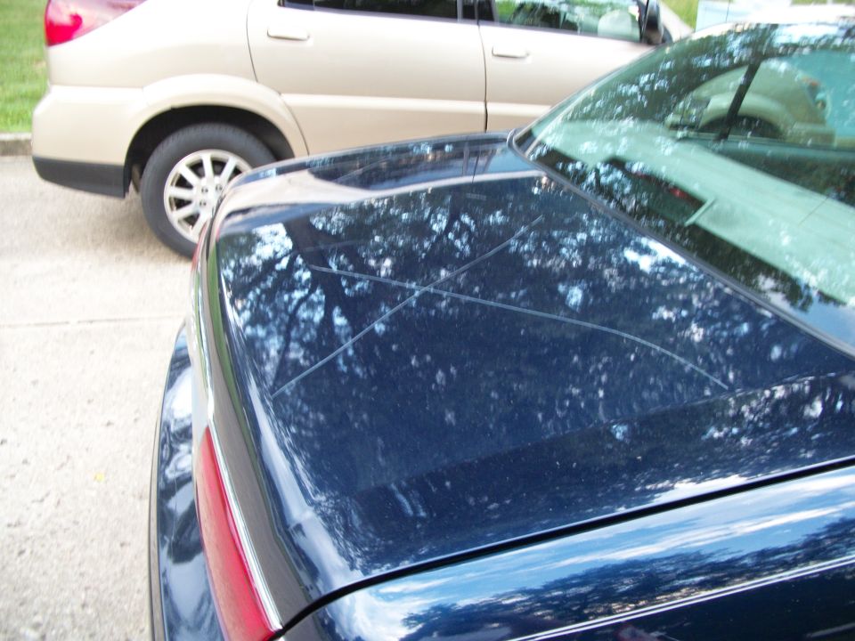 Rear window and decklid of dark blue sedan with tan crossover parked ahead