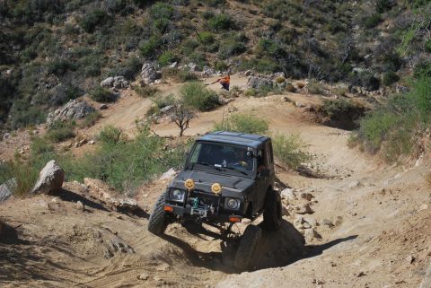 1987 Suzuki Samurai - A Suzuki Samurai navigates a challenging off-road trail with steep inclines and rocky terrain.
