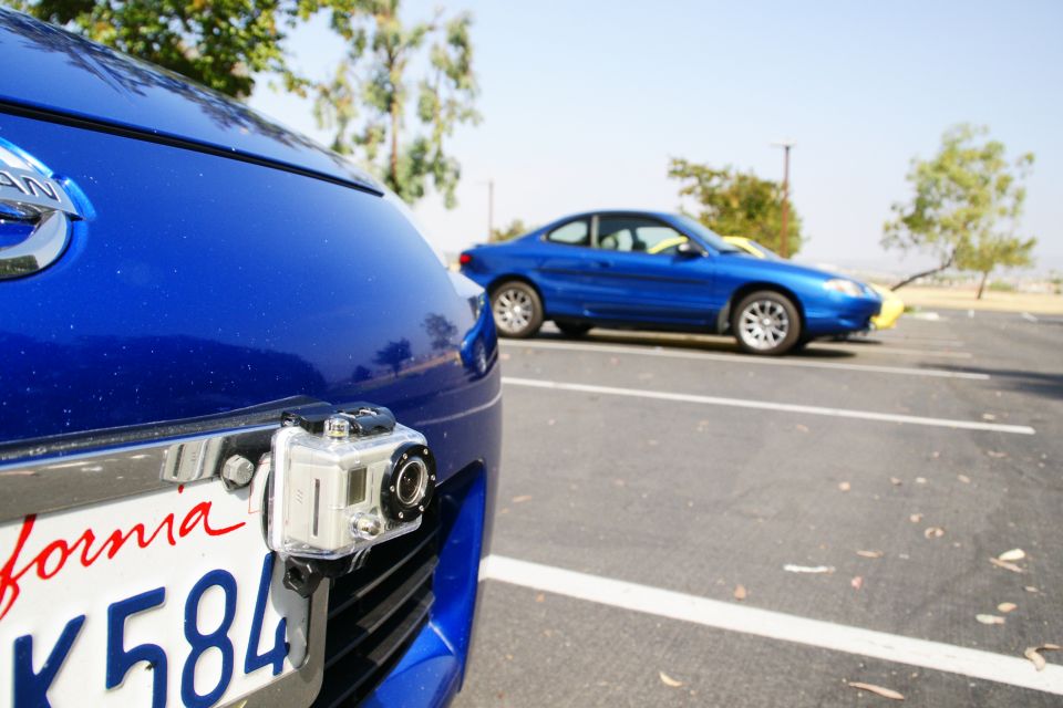 Blue coupe parked in a lot, side view, with a GoPro attached to the front bumper of a blue Nissan