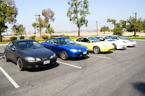 1995 Ford Taurus - A line of Ford Escorts parked in a lot, including a black coupe in the foreground.