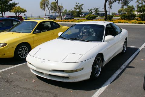 1995 Ford Taurus - A white Ford Probe is parked next to a yellow car in a parking lot on a sunny day.