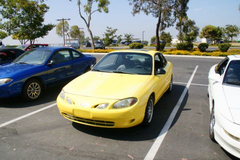 1995 Ford Taurus - A yellow coupe is parked in a lot next to a blue and white car.