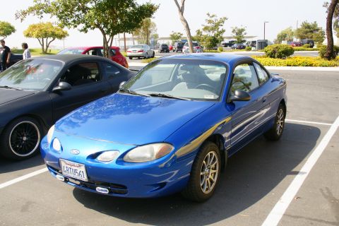 1995 Ford Taurus - A blue coupe is parked in a lot next to another vehicle.