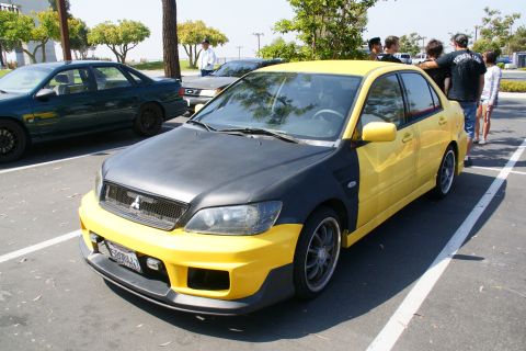 1995 Ford Taurus - A modified Mitsubishi Lancer Evolution with a two-tone yellow and matte black paint scheme is parked in a lot.