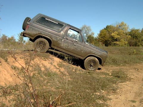 1982 Ford Bronco - This 1980 Ford Bronco is shown off-roading, climbing a steep dirt incline with mud splattered on its body.