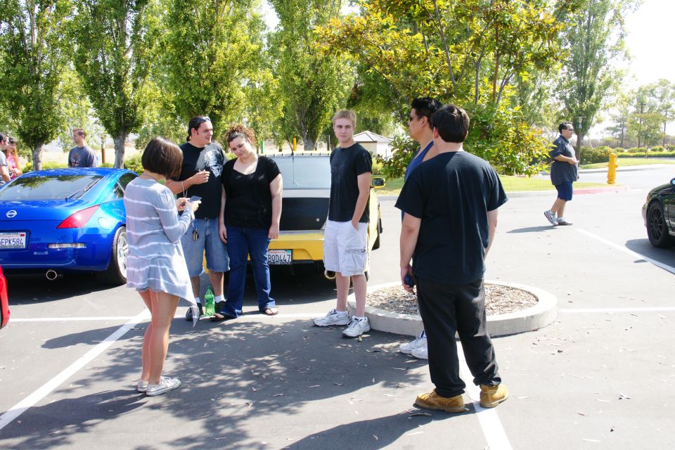People standing around a blue Nissan 350Z and a yellow car in a parking lot