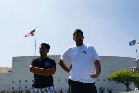 1995 Ford Taurus - Two men stand in front of a building with flags, under a clear blue sky.