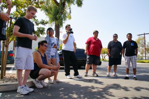 1995 Ford Taurus - A group of people stand around a black sedan in a parking lot on a sunny day.