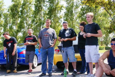 1995 Ford Taurus - A group of people gather around two cars, a blue sports car and a yellow sedan, on a sunny day.