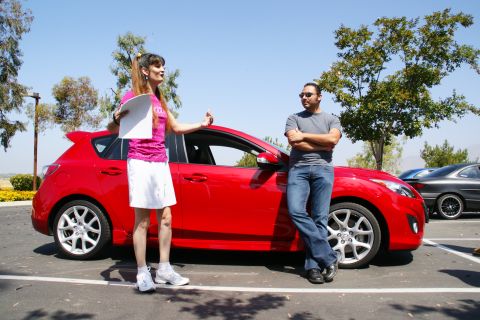 1995 Ford Taurus - A woman gestures while speaking to a man standing by a red car in a parking lot.