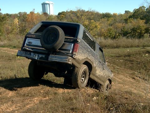 1982 Ford Bronco - This Ford Bronco is navigating a muddy, off-road trail with a water tower in the background.