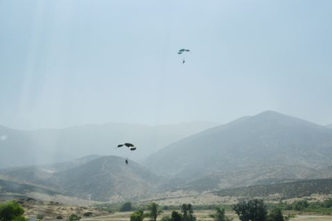 1995 Ford Taurus - Parachutists descend through the hazy sky above a , mountainous terrain.