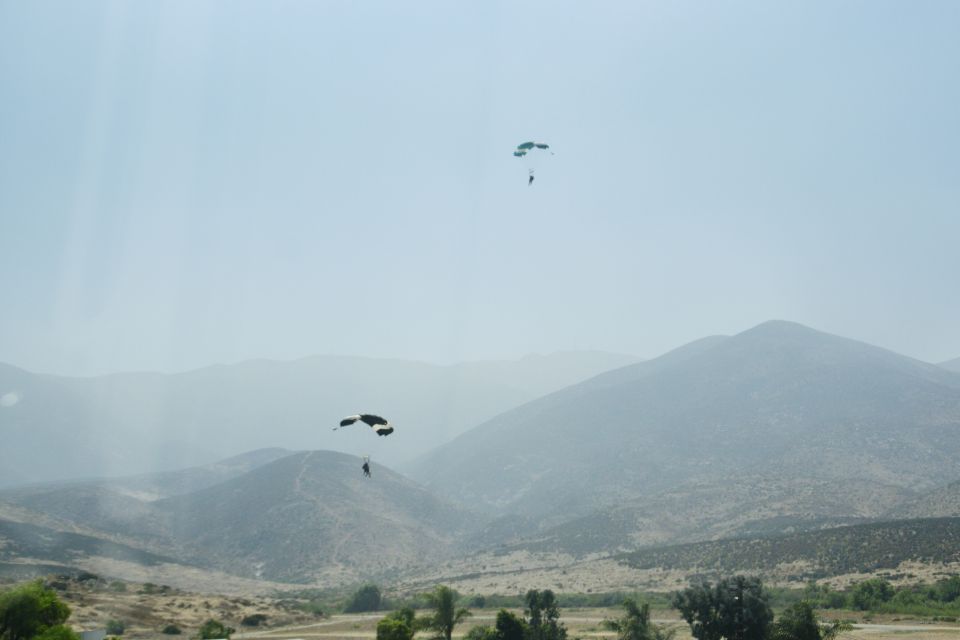 Two people parachuting down towards a dry, mountainous landscape