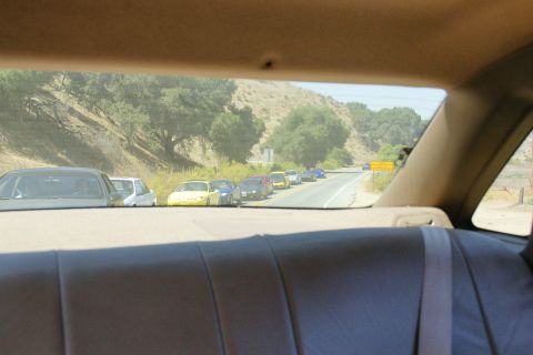 1995 Ford Taurus - A convoy of vehicles travels along a winding road bordered by hills and trees.