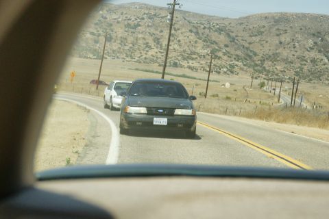 1995 Ford Taurus - A 1995 Ford Taurus drives down a rural highway, with another car visible behind it.