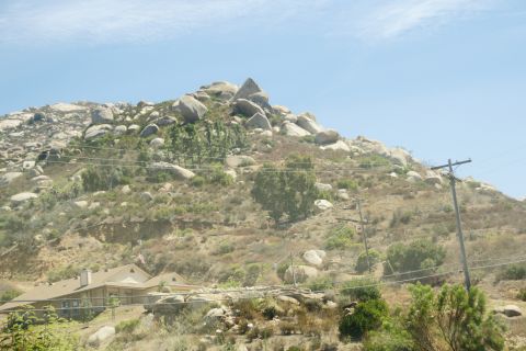 1995 Ford Taurus - A house is visible on a hillside covered in rocks and dry brush, with power lines crossing the scene.