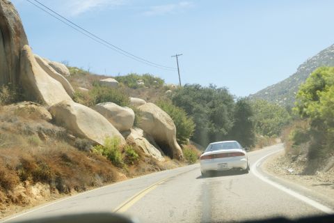 1995 Ford Taurus - A white sedan travels down a two-lane road through a rocky, arid landscape under a clear blue sky.