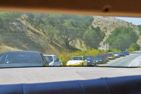 1995 Ford Taurus - A convoy of cars travels down a highway on a sunny day, with hills and vegetation lining the road.