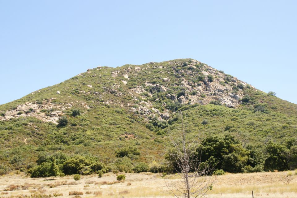 Mountain covered in green brush and rocks under a clear blue sky