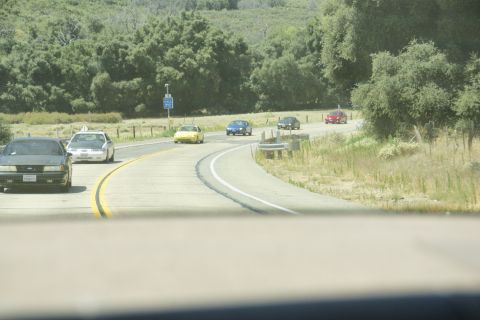 1995 Ford Taurus - Multiple vehicles travel along a highway with trees and hills in the background.