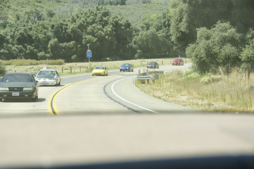 Several cars driving on a winding road through a hilly, wooded area