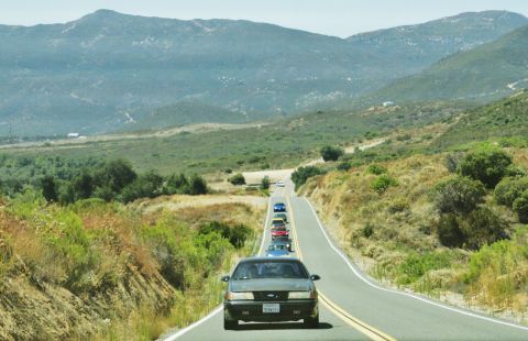 1995 Ford Taurus - A procession of vehicles travels along a winding road through a hilly, arid landscape.