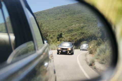 1995 Ford Taurus - A 1995 Ford Taurus is seen from a side mirror driving on a winding road with another vehicle following.