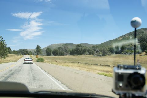 1995 Ford Taurus - A white 1995 Ford Taurus travels down a highway surrounded by dry grass and hills under a blue sky.